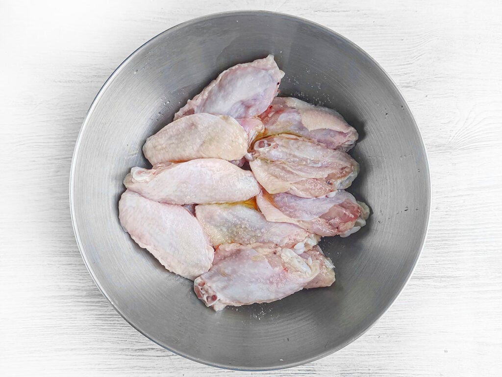 Raw chicken wings in a silver bowl.