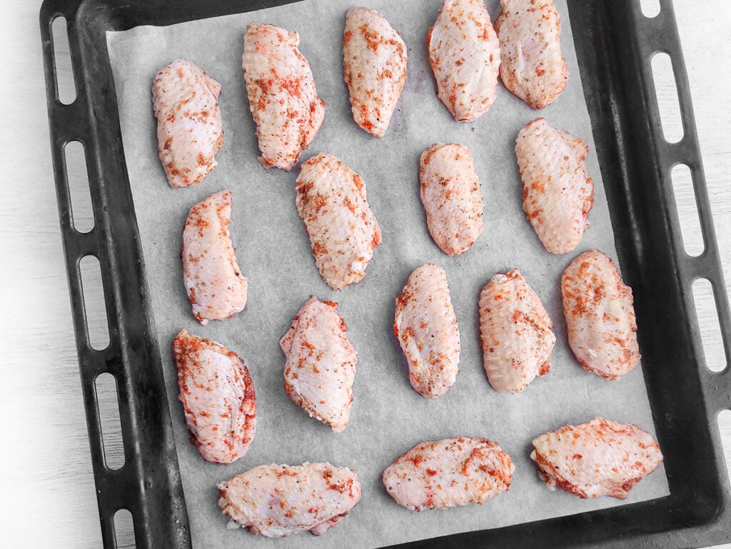 Raw, seasoned wings on a baking tray with parchment paper underneath.