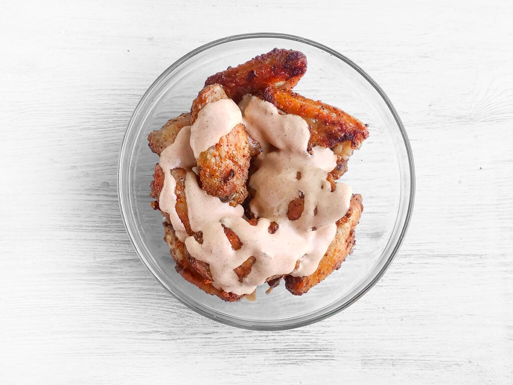 Crispy baked wings with buffalo ranch sauce drizzled over top, ready to be tossed.