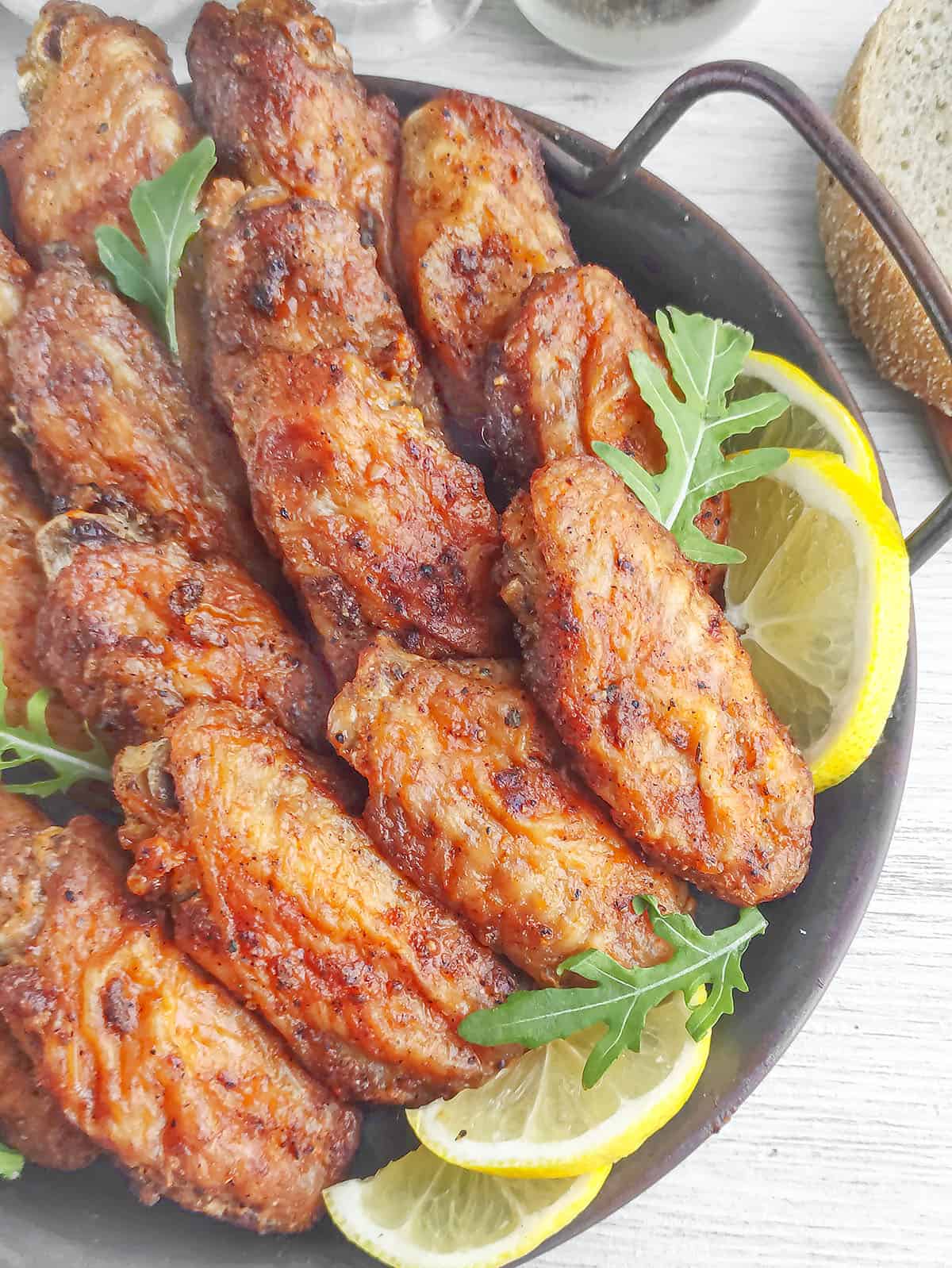Buffalo ranch wings in a black plate with lemon slices.