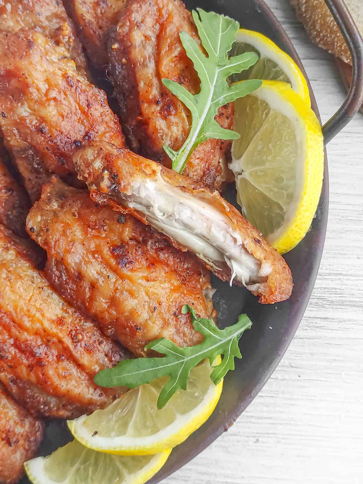 Buffalo ranch wings on a serving platter with lemon wedges and greens. There is a bite taken out of one baked wing.