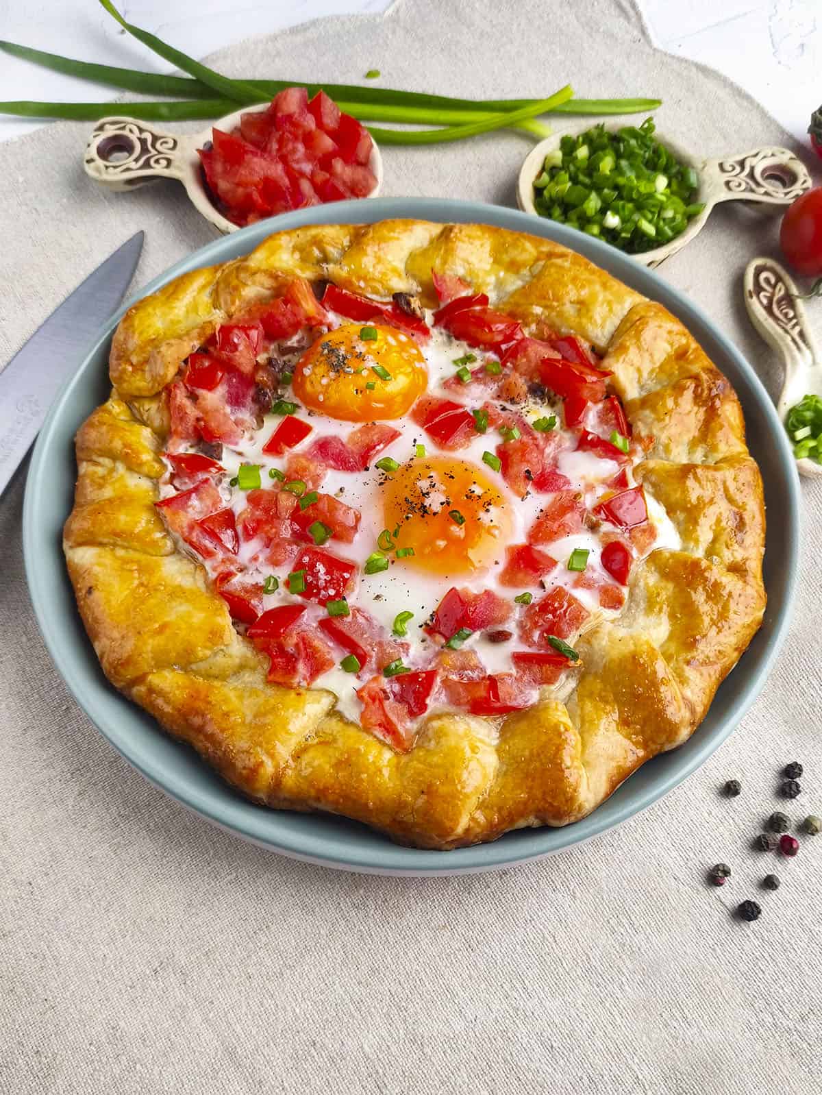 The breakfast galette on a linen tablecloth with toppings in bowls above it.