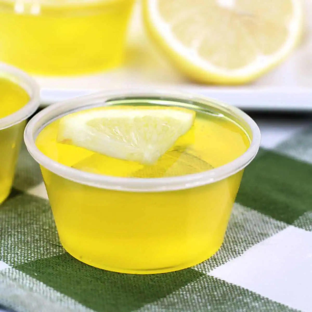 A lemon jello shooter in the front on a green checked napkin.