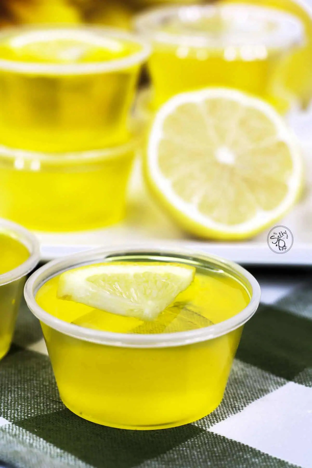 Lemon jello shooters stacked on a white plate with one shooter in the forefront.
