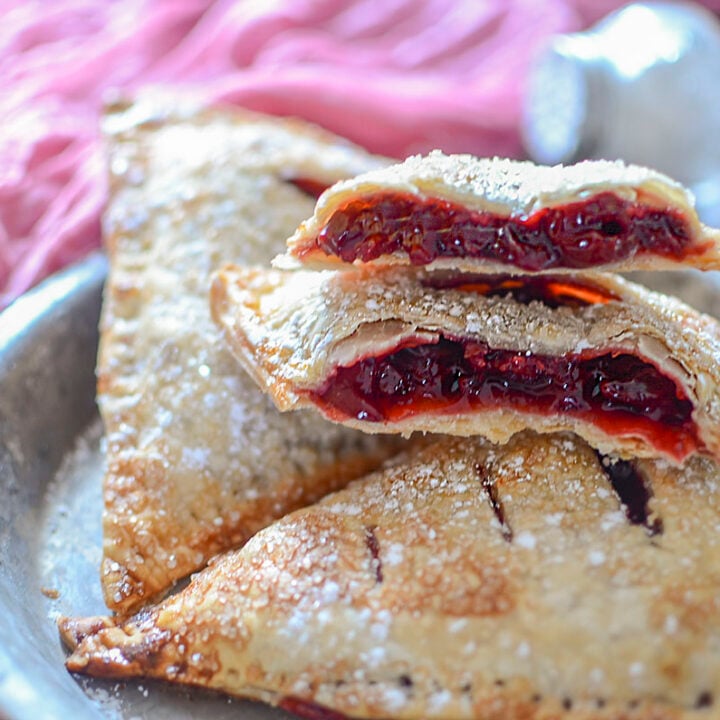 Cherry hand pies on a plate with one hand pie open to show the filling.