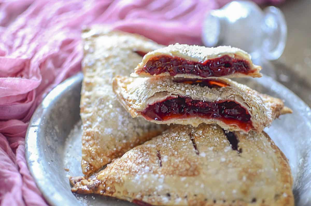 Cherry hand pies on a plate with one hand pie open to show the filling.
