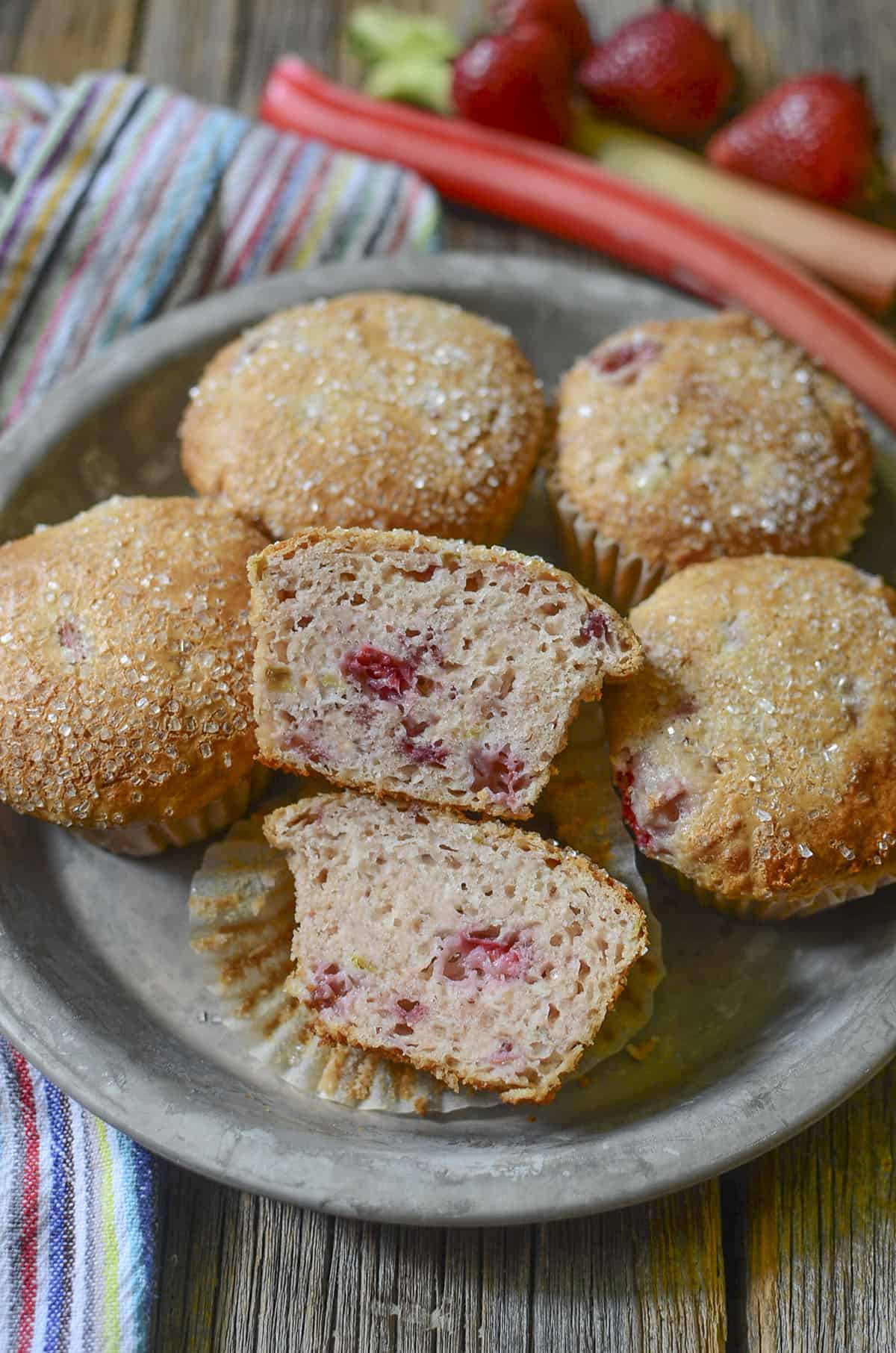 5 muffins sitting in a tin plate pan with sticks of rhubarb on the upper right.
