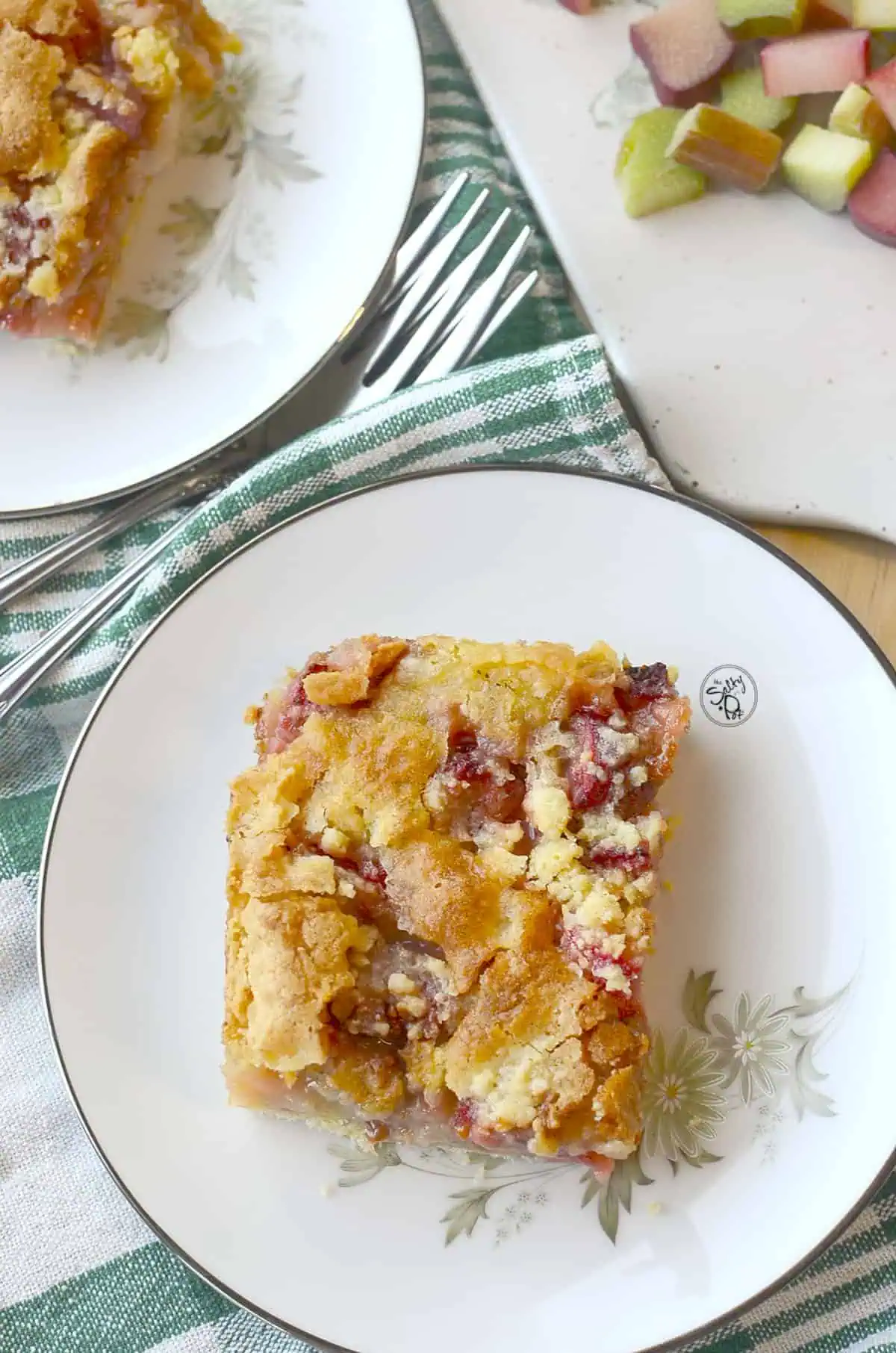 Strawberry rhubarb crumb bars in china plates with a green napkin underneath.