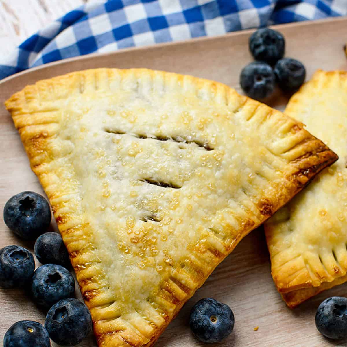 Blueberry hand pies with blueberries around it. Square image.