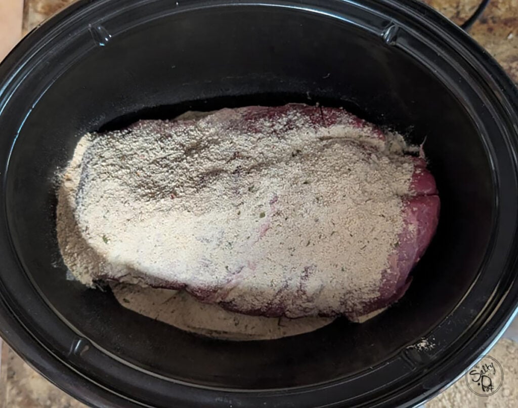 The roast with the seasoning sprinkled over top in the slow cooker.