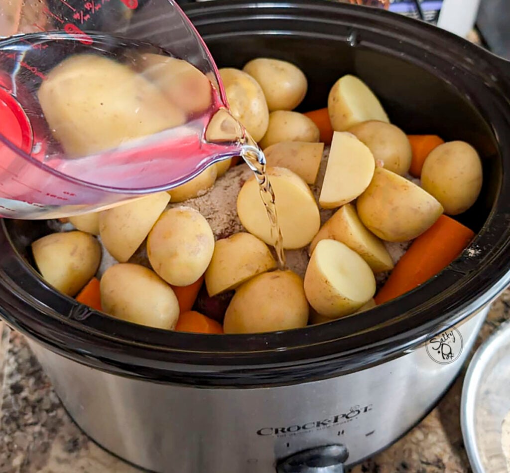 Adding water to the pot after the veggies have been put on top of the roast.