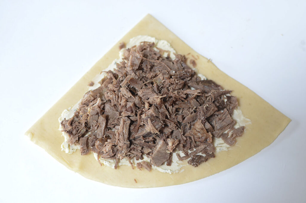 Roast beef is places on top of the seasoned cheese on the pastry section.