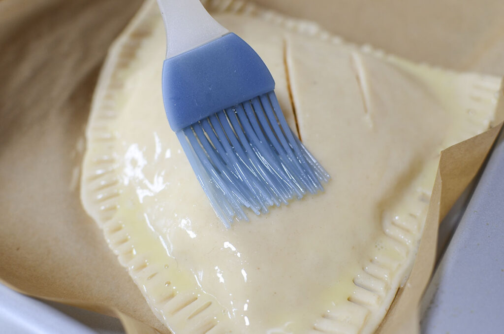 Egg wash is brushed on top of the hand pie with a blue silicone brush.