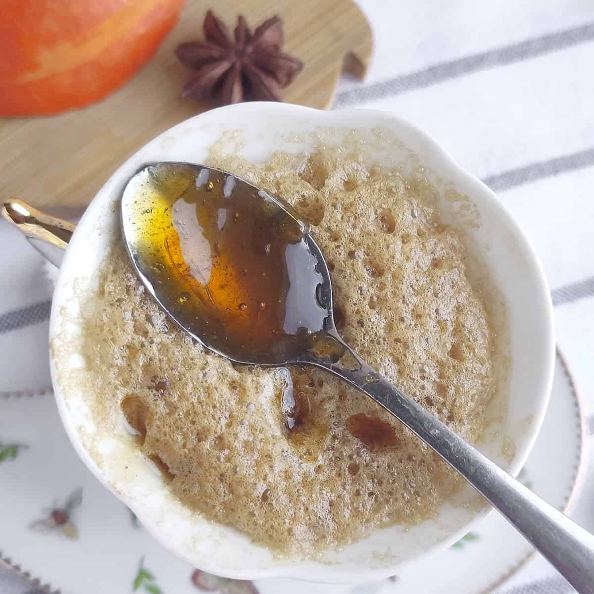 Pumpkin spice syrup on a spoon resting on top of foamed coffee.