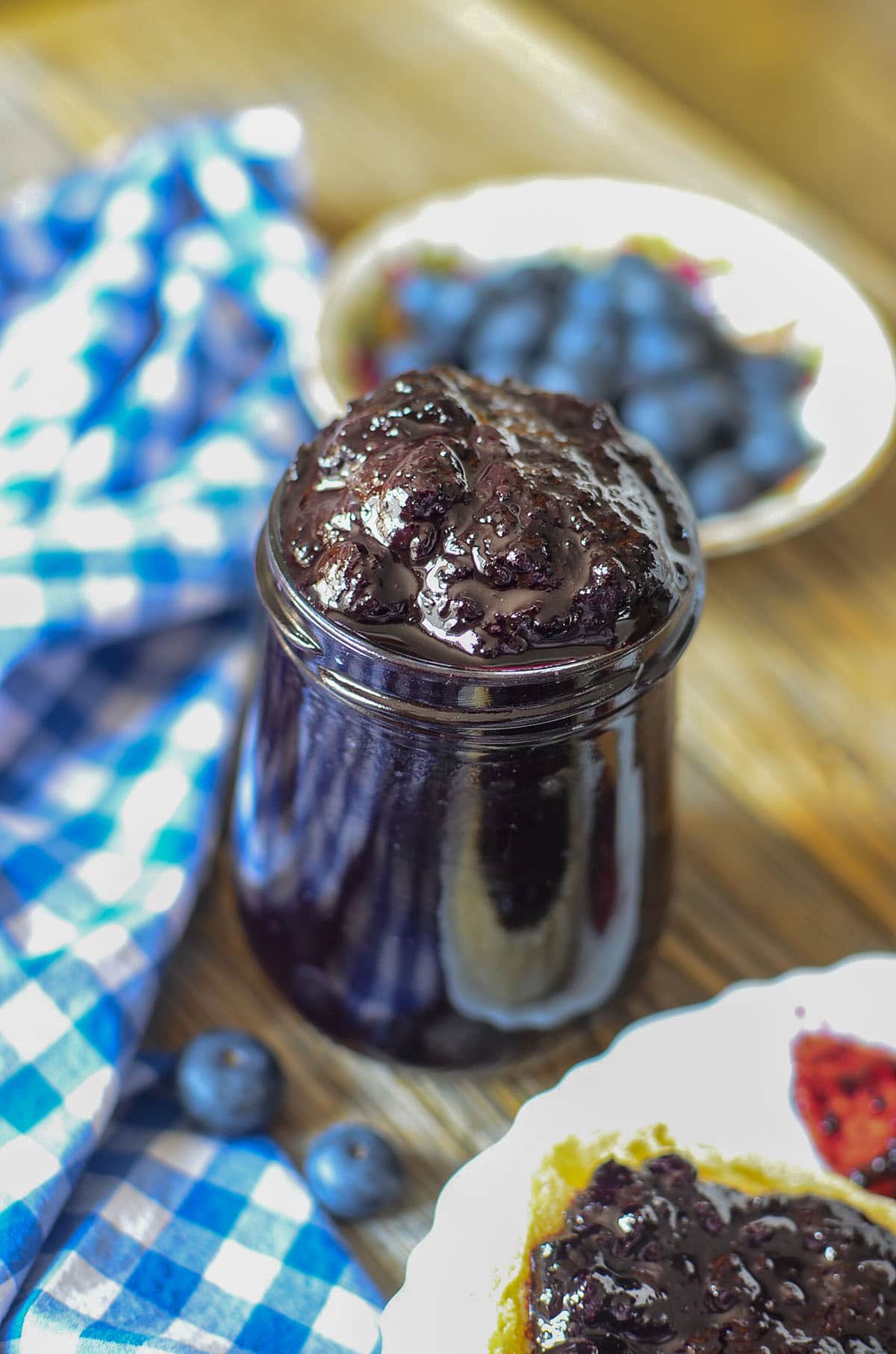 Blueberry butter in a glass jar with a blue and white napkin next to it.