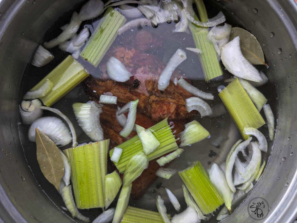 Water, smoked pork hock and soup veggies in a soup pot.