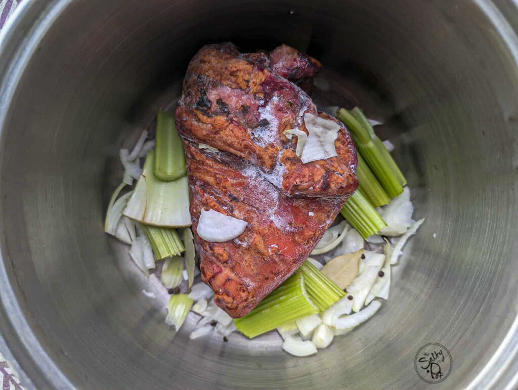 A smoked pork hock in a pot with raw veggies around it.
