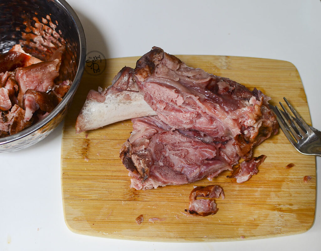 A cooked pork hock with the meat off the bone on a wooden cutting board.