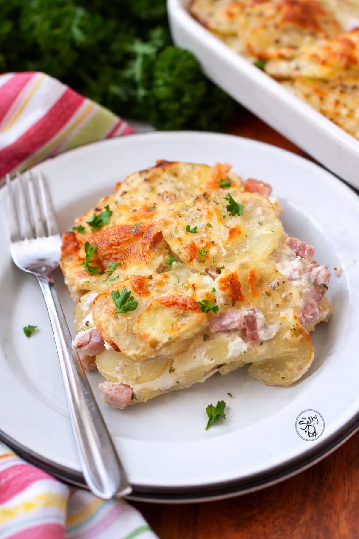 A portion of scalloped potatoes with ham on a white plate. there is a fork on the plate on the left.