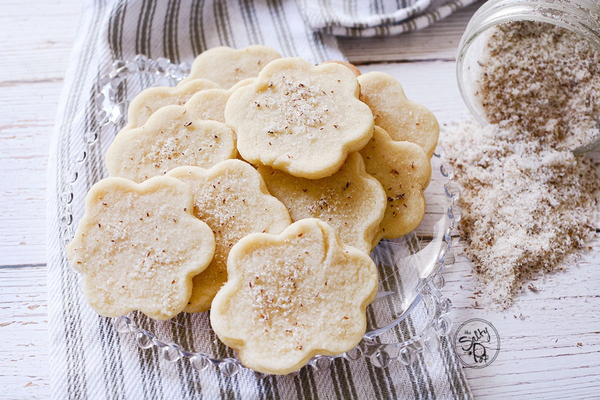 Lilac Cookies on a plate with lilac sugar spilling out of a jar beside it. 