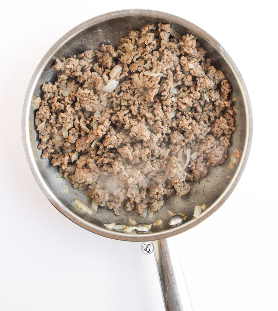 Ground beef browning in a skillet with onions for baked beef tacos.