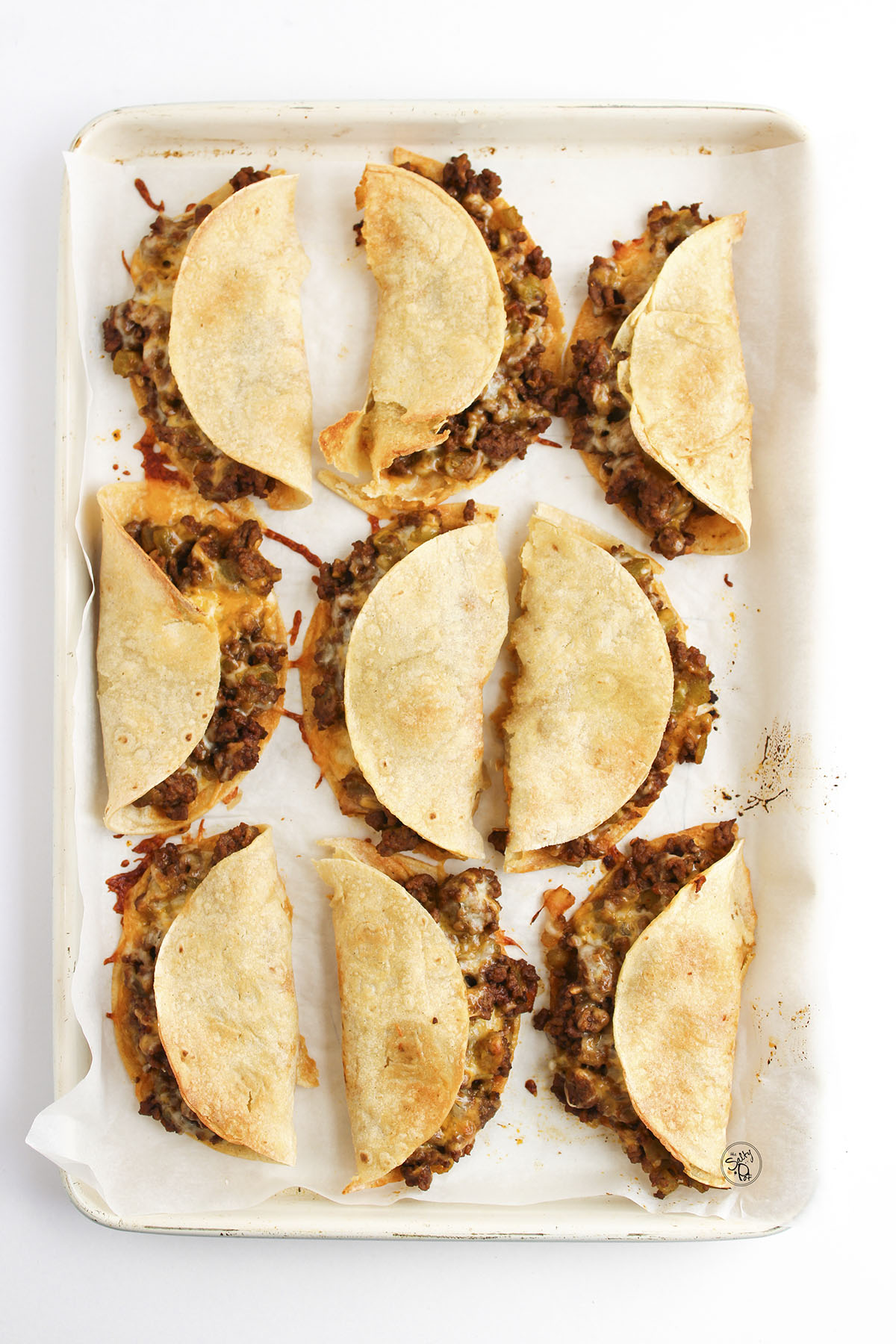 Folded beef tacos on baking sheet brushed with oil before baking.