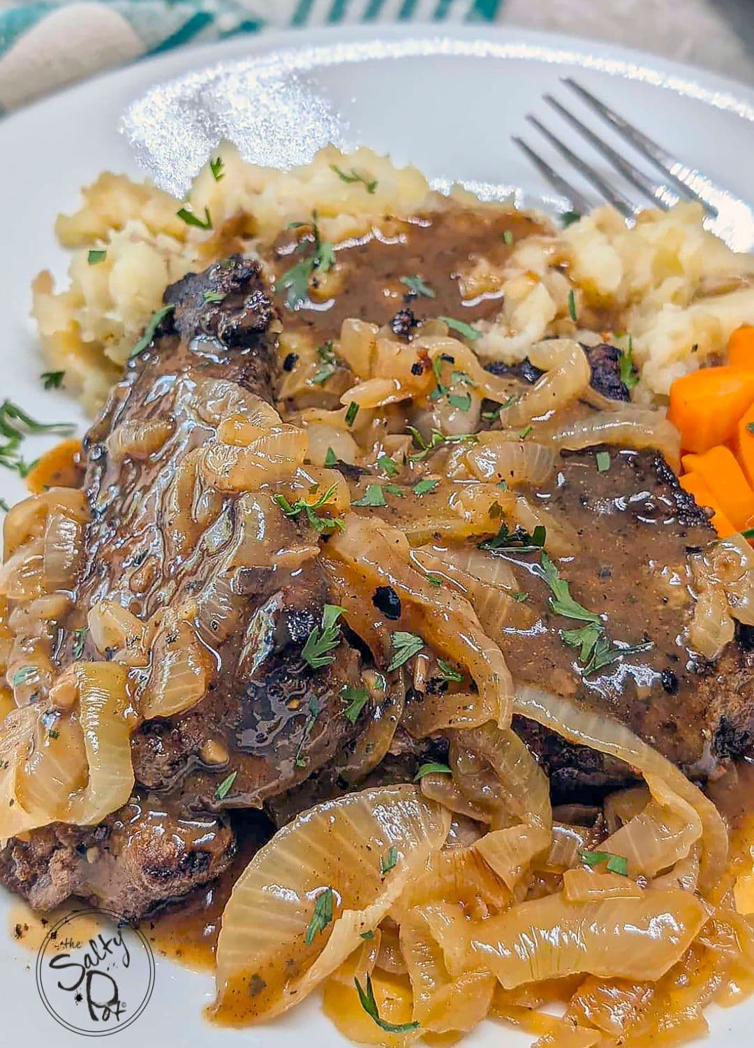 Liver and onions with gravy served on a plate with carrots and mashed potatos