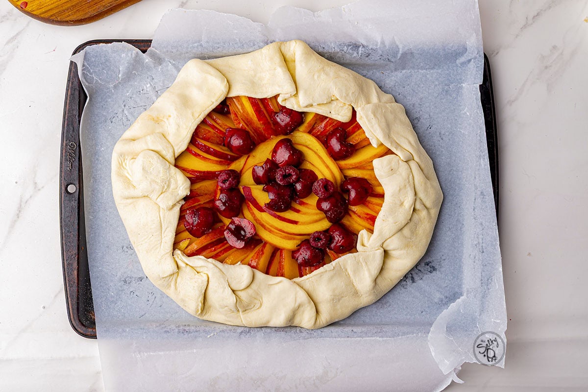 The galette with folded edges to keep the fruit and juices in, sitting on parchment lined baking dish.