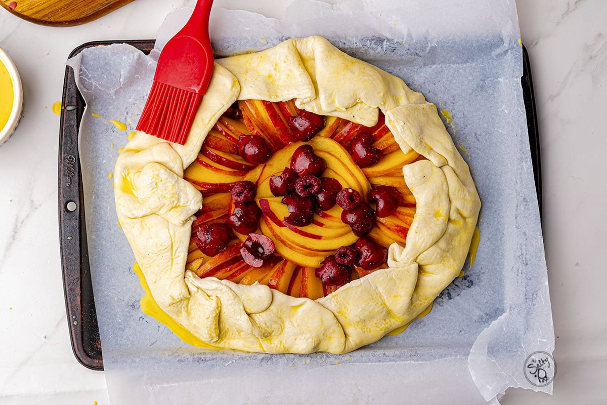 A silicone brush (red) brushing on egg wash to the top of the galette.
