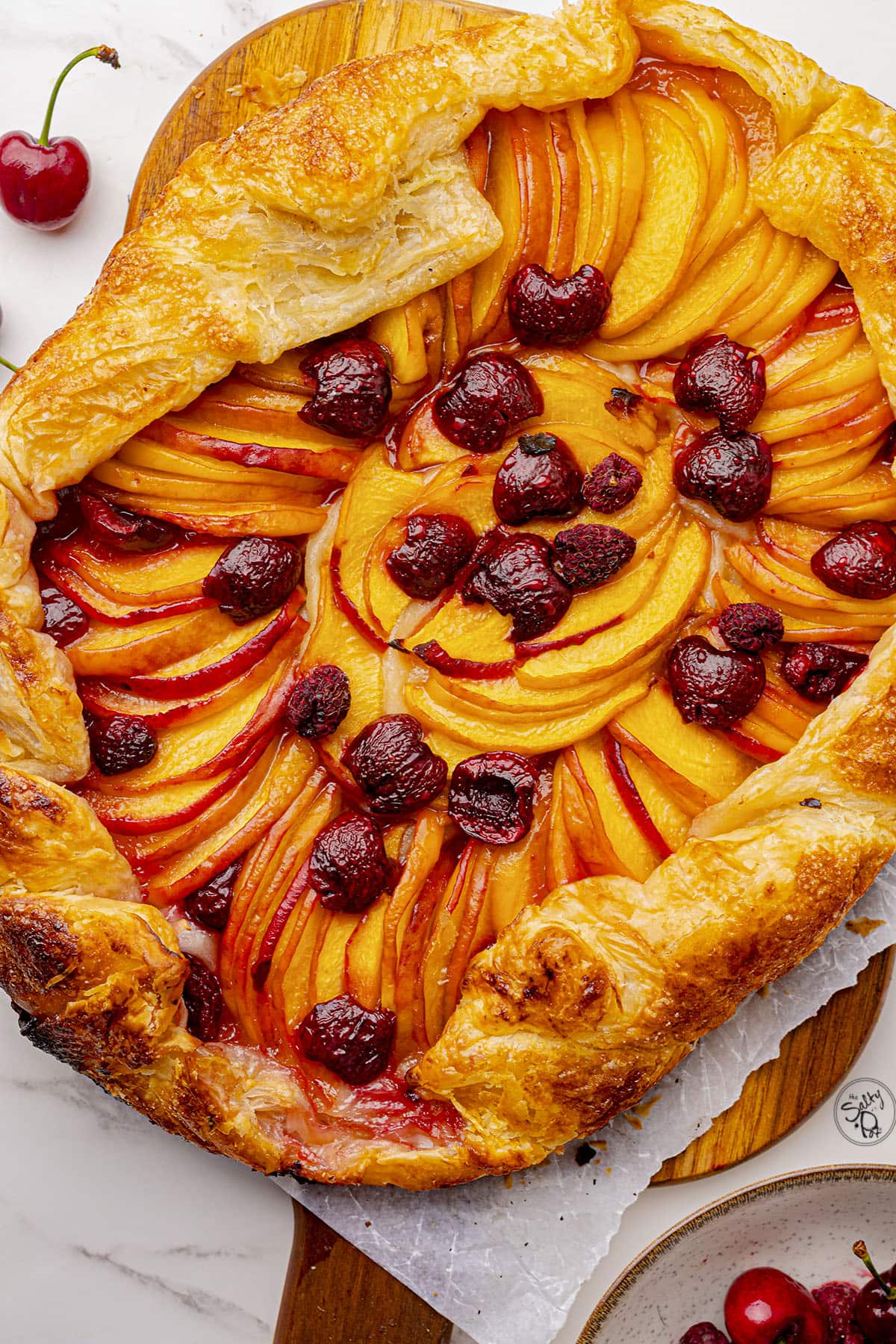A fruit galette on a wooden cutting board, cooling.