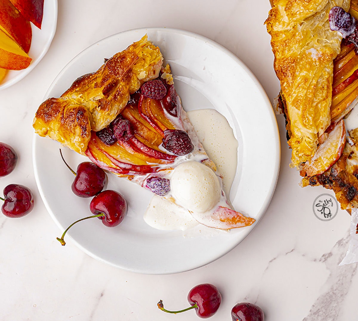 One slice of the galette with ice cream on top. Cherries are dotted around the frame.
