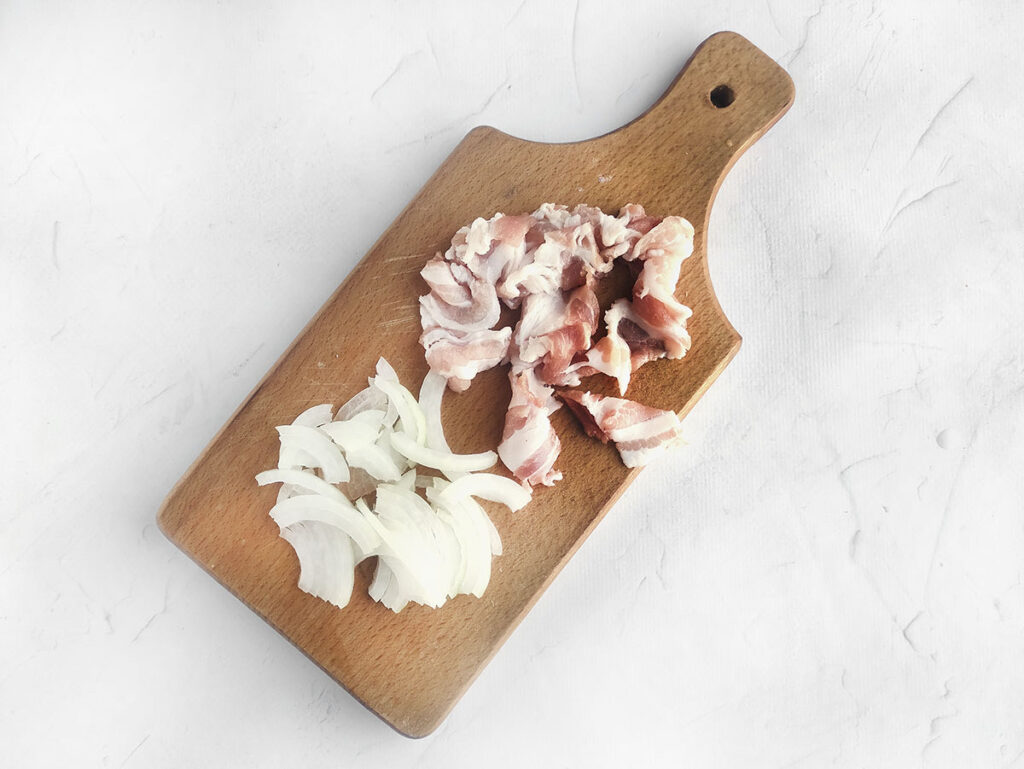 Chopped onion and bacon on a wooden chopping board.