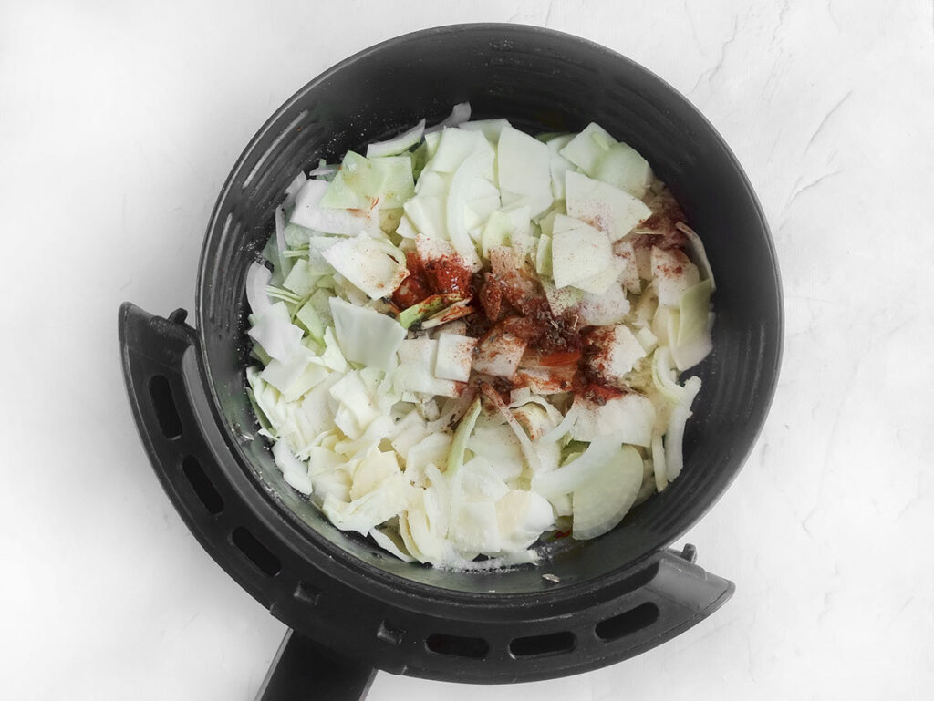 Chopped cabbage in the air fryer with spiced on top. 