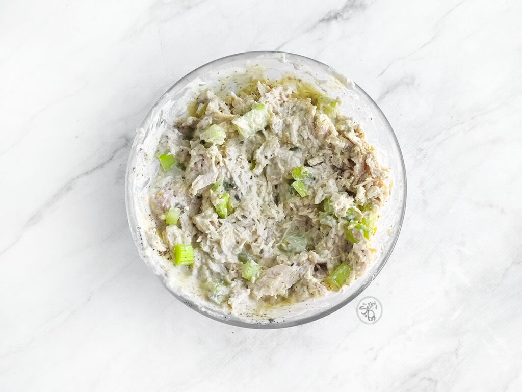 The final chicken salad mixture in a glass bowl, showing the shredded chicken and celery perfectly coated in the creamy, herb-speckled ranch dressing.