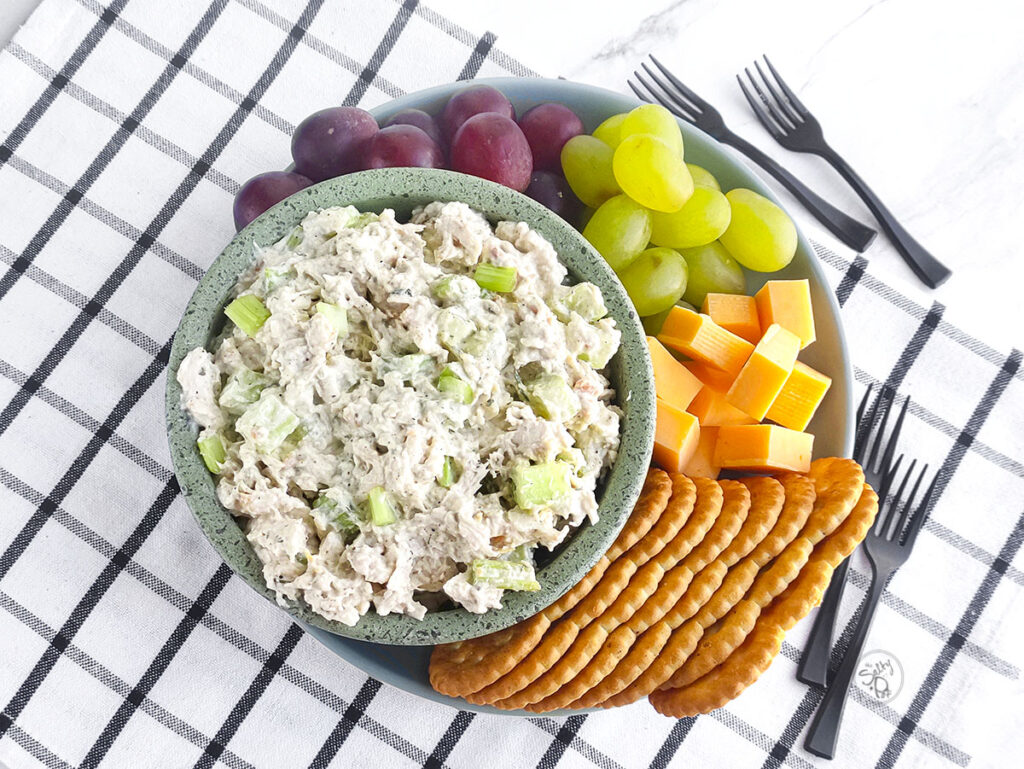 Ranch chicken salad in a bowl on a platter of crackers, cheese and grapes.