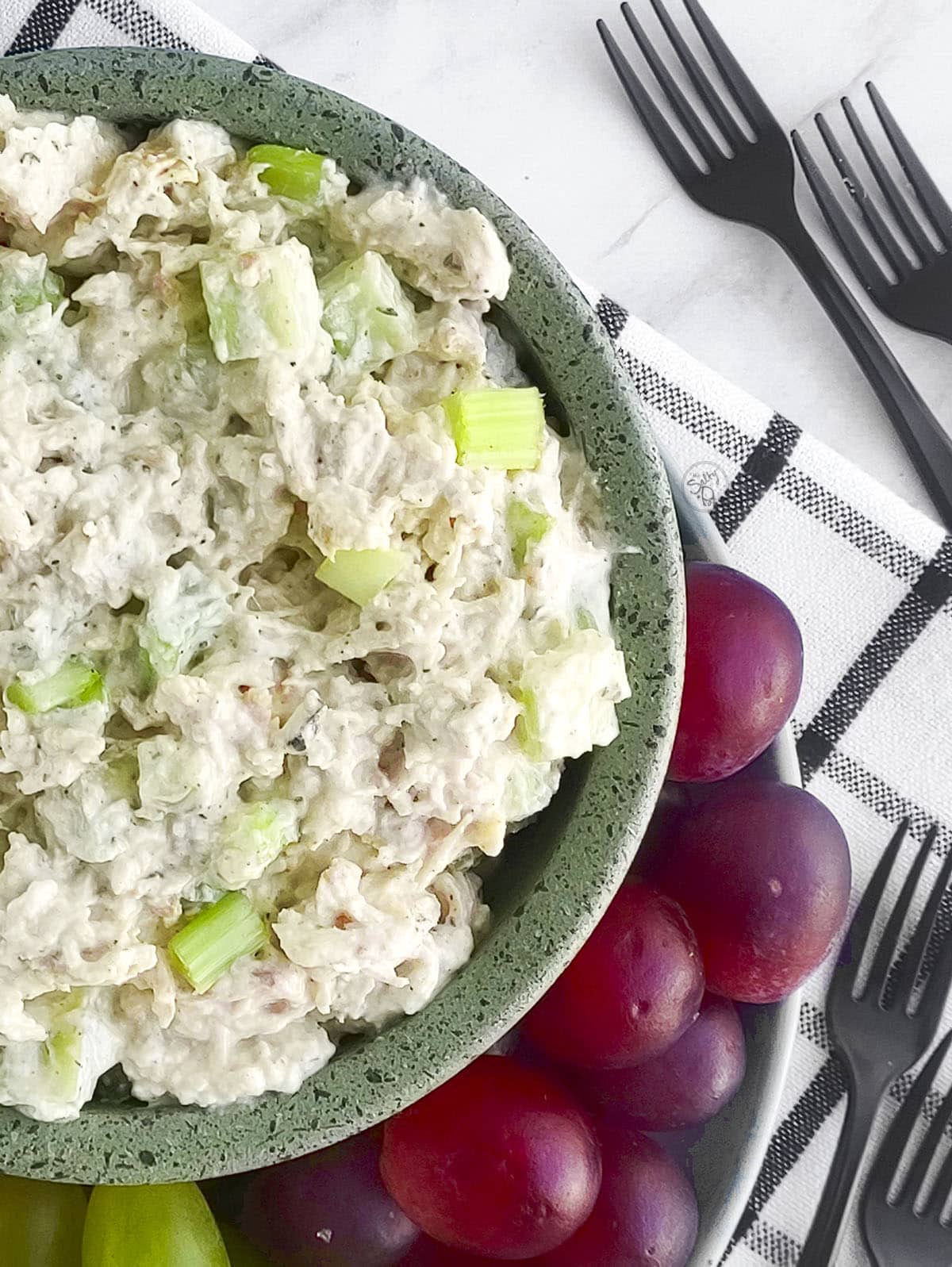 An extreme close up of the ranch chicken salad in a green bowl with red grapes on the side. 