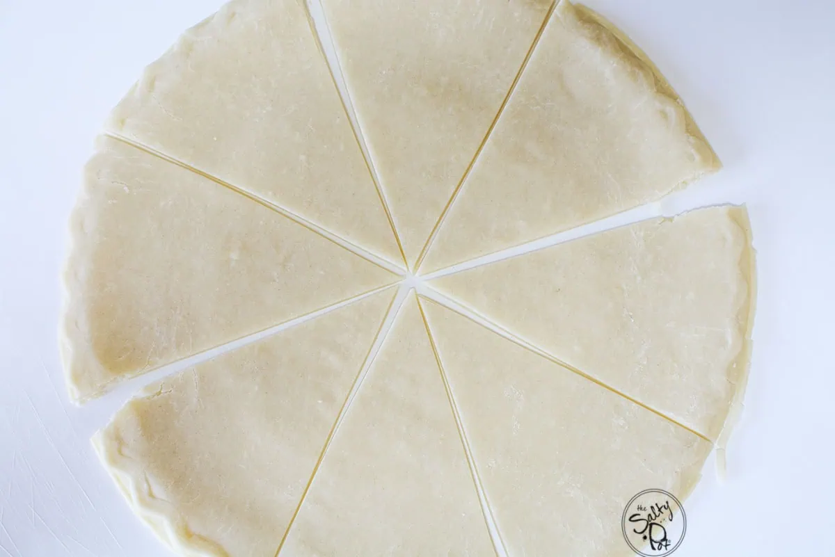 A top-down view of a circular store-bought pie crust cut into eight even, triangle-shaped wedges on a clean white surface.