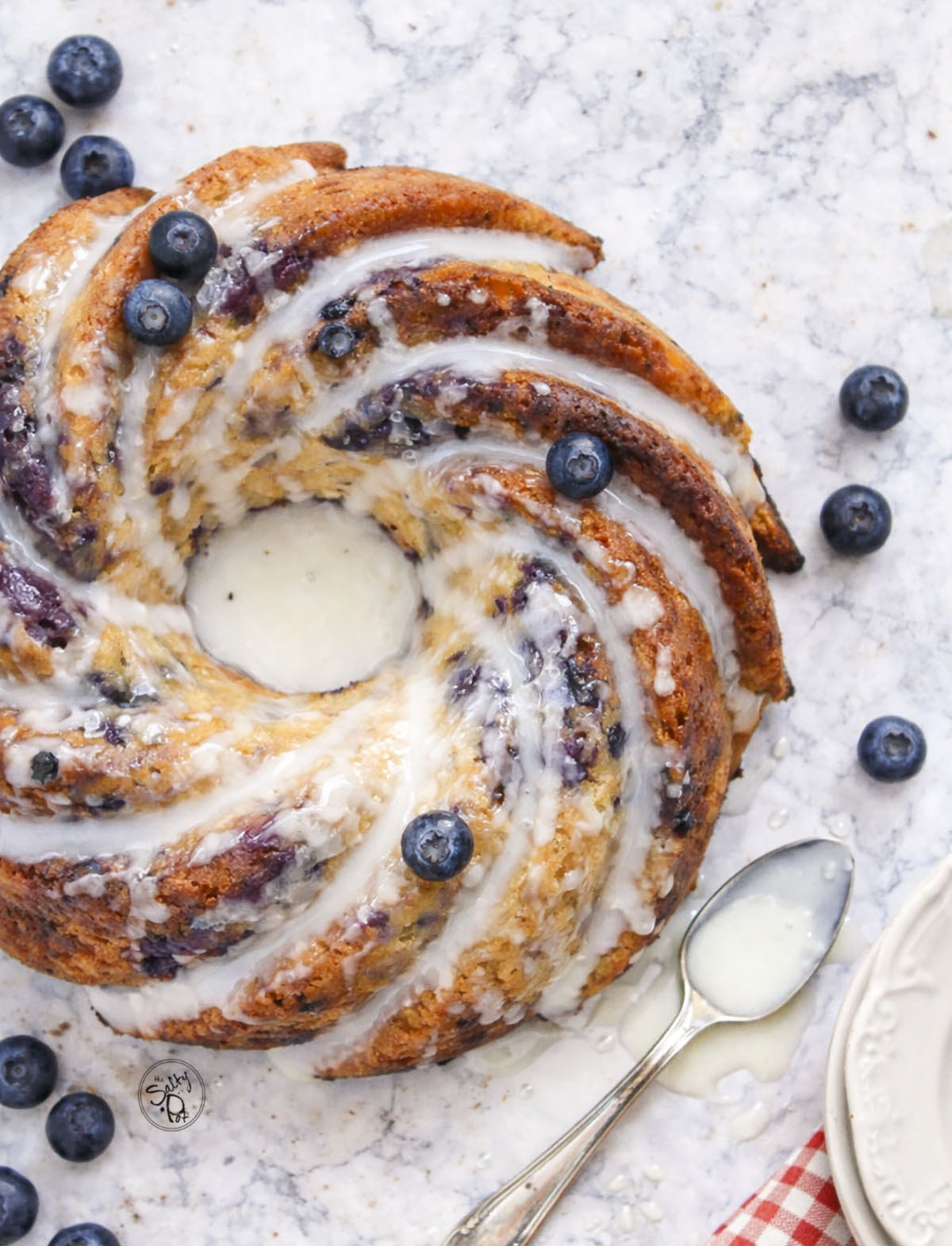 A top-down view of the glazed bundt cake, highlighting the swirls of the pan and the vibrant purple blueberry pockets throughout.