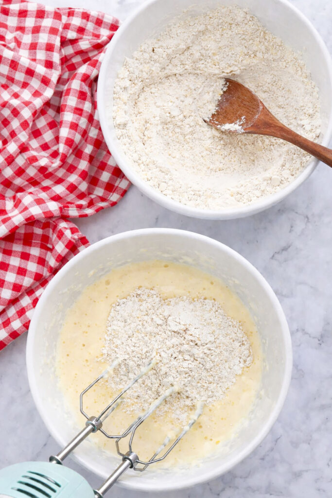 A white bowl showing the creamed butter and sugar mixture being combined with dry flour ingredients using a hand mixer.