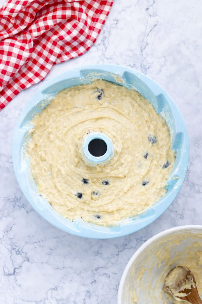 The lemon blueberry cake batter poured into a greased light blue silicone bundt pan, ready for the oven.