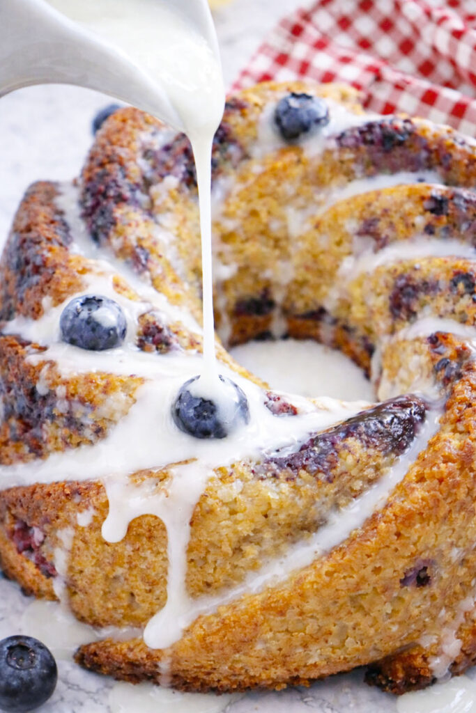 A close-up of a white glaze being drizzled over the top of the freshly baked golden-brown bundt cake.