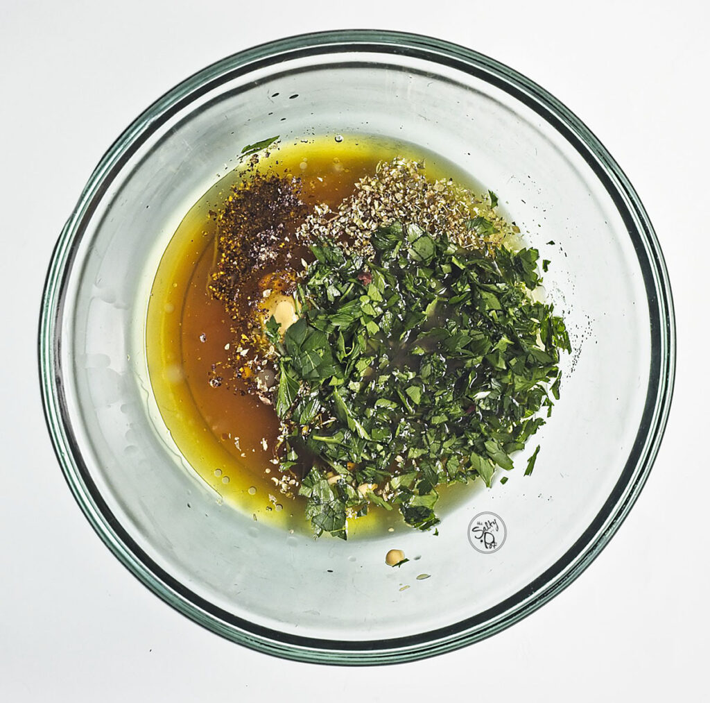 Small glass bowls containing the Greek dressing ingredients: olive oil, red wine vinegar, lemon juice, Dijon mustard, and dried oregano.