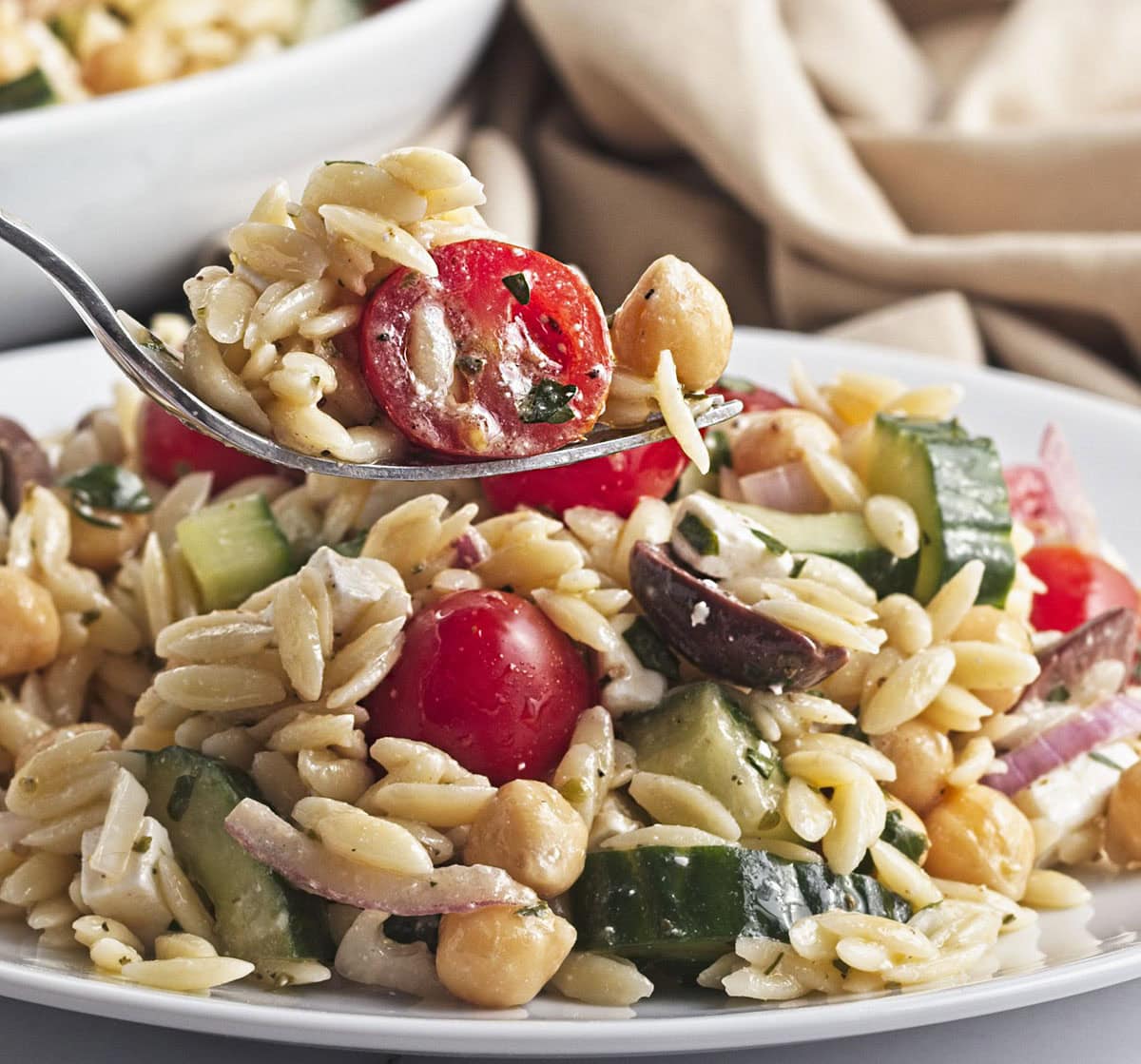 Chickpea orzo salad on a fork above the plate.