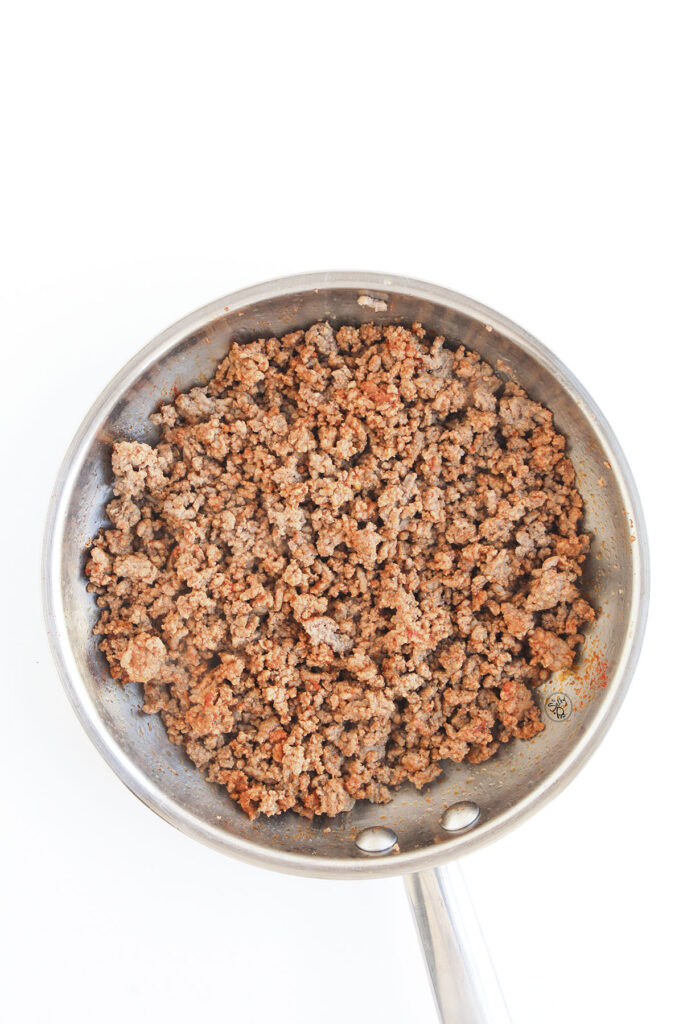 Cooked ground beef being browned and seasoned in a stainless steel skillet.