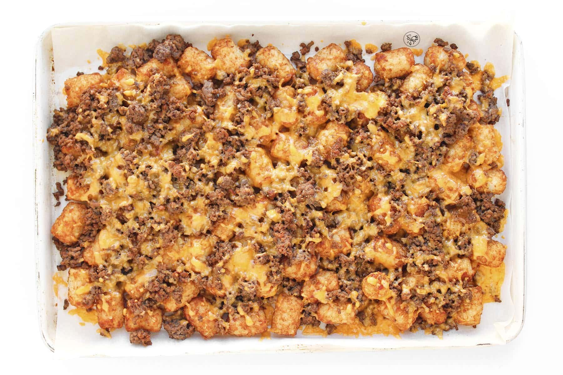 A sheet pan of tater tots and beef with a thick, bubbly layer of melted cheddar cheese fresh from the oven.