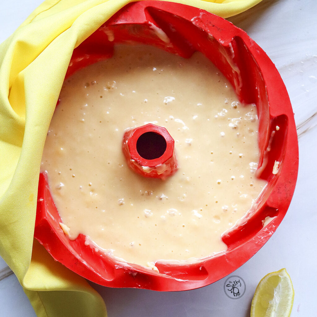 Smooth, pale yellow lemon cake batter filled to the top of a bright red fluted silicone bundt pan.