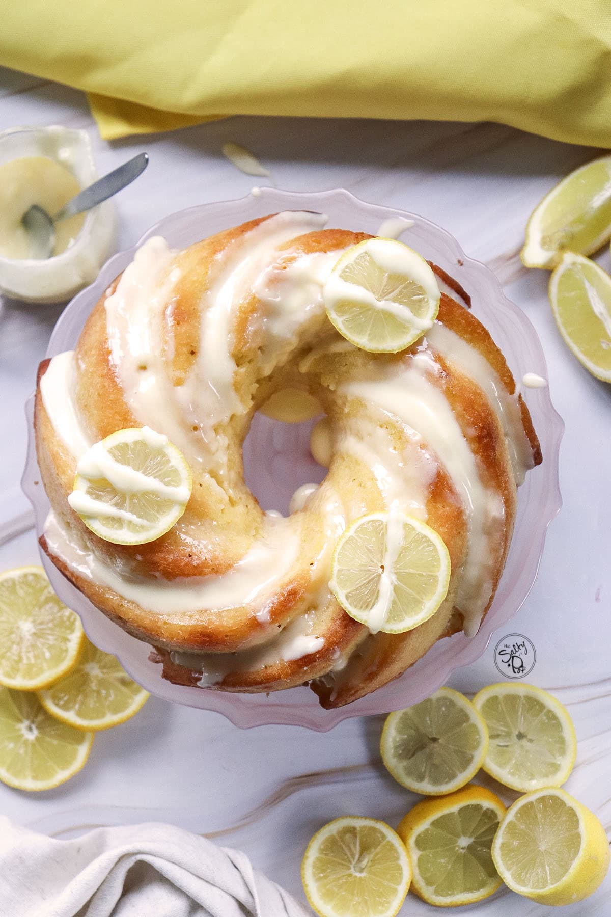 An overhead "hero" shot of the finished lemon cake with a thick white glaze dripping down the sides, accented by thin lemon wheel garnishes.