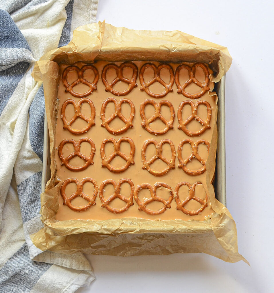 The bars in the pan after a smooth, melted butterscotch layer has been poured over the top and topped with rows of whole pretzel twists.