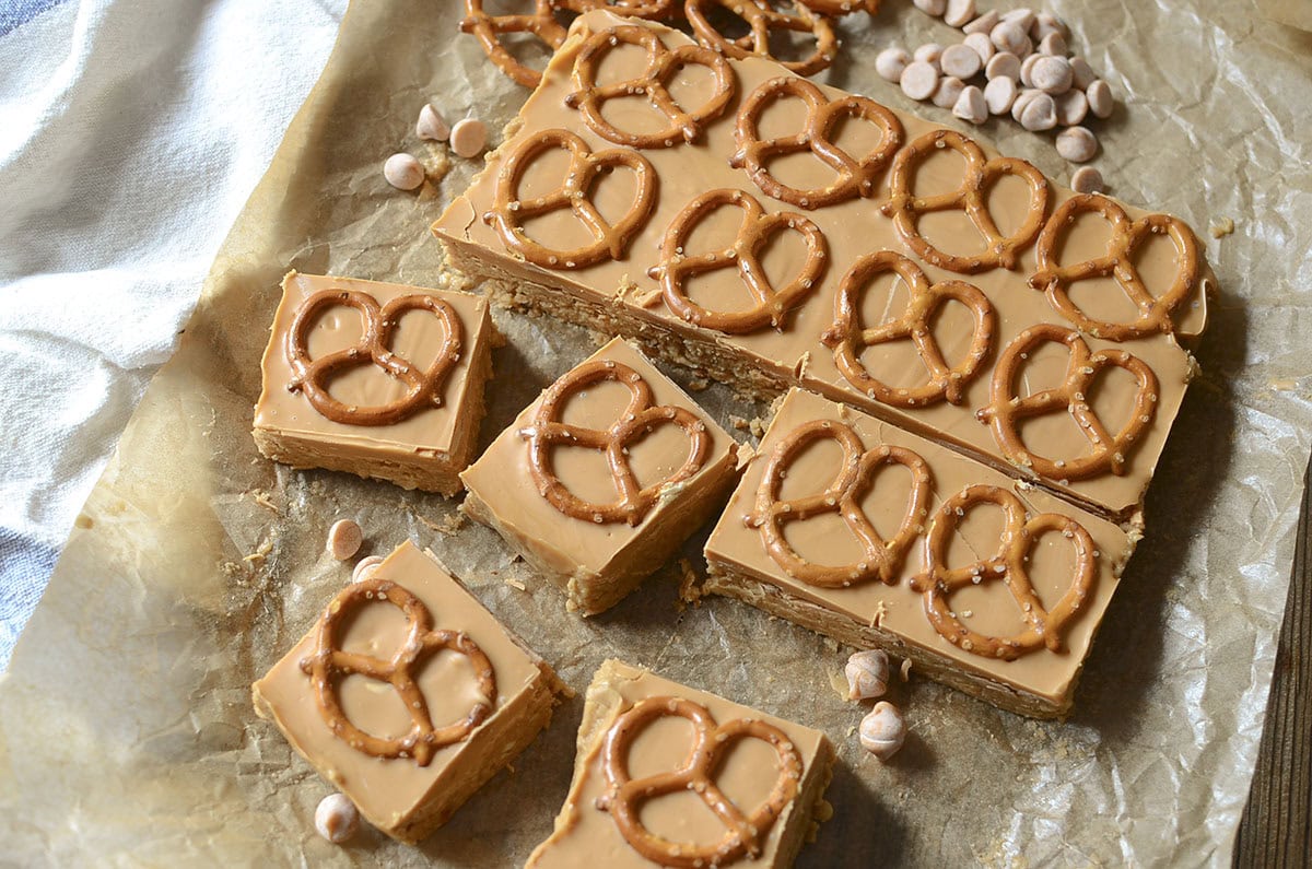 A close-up, slightly angled view of the sliced bars, highlighting the texture of the base and the glossy butterscotch topping, surrounded by loose butterscotch chips and pretzels.