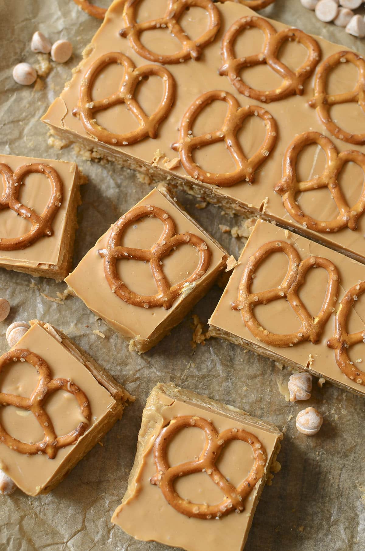 A vertical shot of the finished bars lifted out of the pan on parchment paper. Several squares have been cut, showing the thick peanut butter base and the smooth butterscotch top with a pretzel.